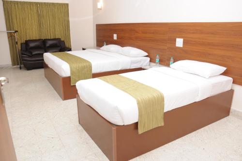 a hotel room with two beds and a chair at Sreeparthi Hotel in Puttaparthi