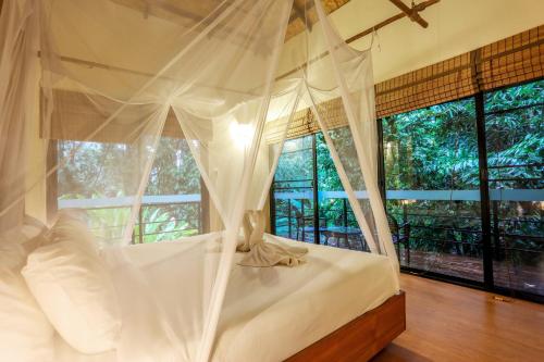 a bedroom with a white canopy bed with a window at Anurak Community Lodge - SHA Plus in Khao Sok