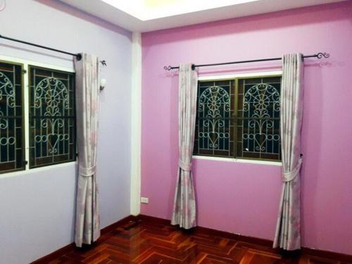 Cette chambre est dotée de murs roses et de 2 fenêtres avec des rideaux. dans l'établissement Single House Sattahip, à Sattahip