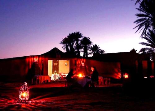 un grupo de personas sentadas frente a una casa por la noche en Nomad Life Style en Mhamid