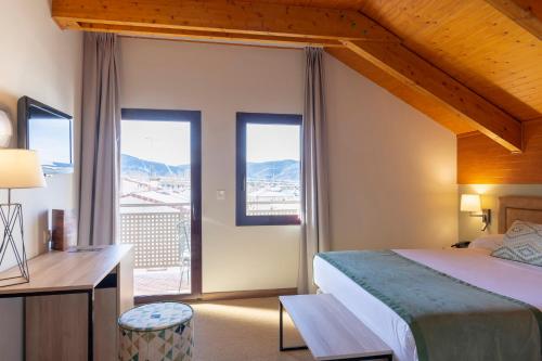 Un dormitorio con una cama y un escritorio y ventanas. en Hotel & Spa Real Jaca, en Jaca