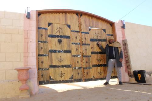 Un uomo in piedi davanti a una grande porta di legno di Maison Proche De Désert Douz a Douz