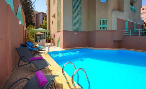 馬拉喀什的住宿－Appart-Hotel Amina Resort，一座大型游泳池,旁边是一座建筑,配有紫色椅子