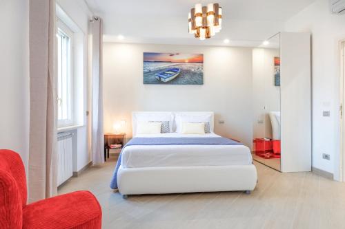 a white bedroom with a bed and a red chair at Appartamento Sorrento Sunrise in Sorrento