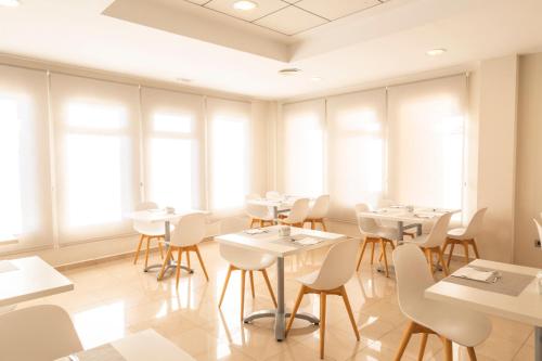 a restaurant with white tables and chairs and windows at Hotel Cristina in Los Alcázares