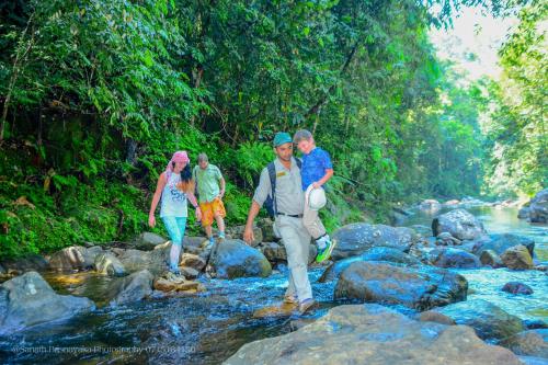 a group of people walking across rocks in a river at Rainforest Holiday Inn in Deniyaya