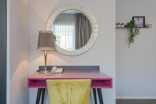 a pink desk with a lamp and a mirror at Hotel Op Diek in Den Hoorn