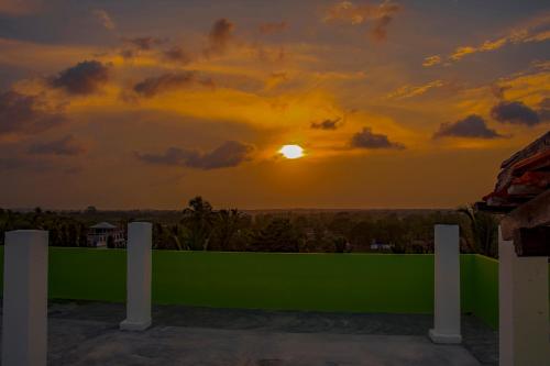 a sunset over a green fence with the sun in the sky at Nice Place Beach Hotel in Arugam Bay
