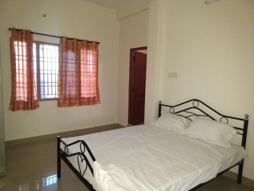 a bedroom with a bed with white sheets and a window at STHALAS in Mahabalipuram