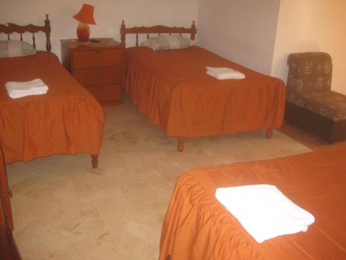 a room with two beds with orange sheets and a dresser at Hostal Camiluz in Nazca