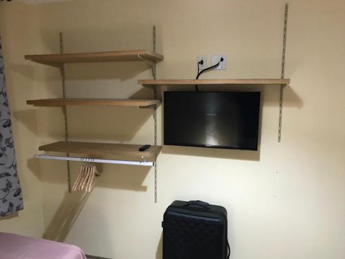 a room with a tv and shelves and a suitcase at GA1-Hospedagem Próximo ao Aeroporto de Guarulhos in Guarulhos
