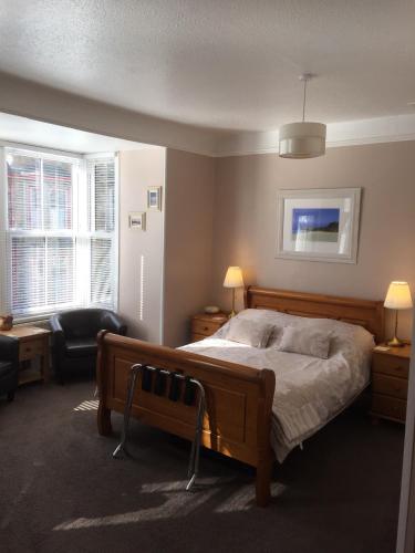 a bedroom with a bed and a chair and two windows at Chiverton House Guest Accommodation in Penzance