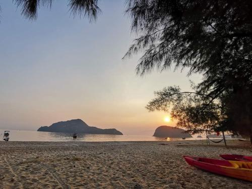 a sunset on a beach with a surfboard on the sand at บ้านพักน้องจ็อบ in Baanphakrimlay 