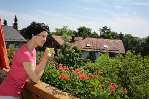a woman standing on a balcony drinking a cup of coffee at Appartementhaus Albrecht in Bad Füssing