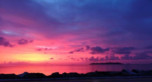 a sunset over the ocean with rocks in the foreground at Nisaki Hotel & Elite Suites in Ermoupoli