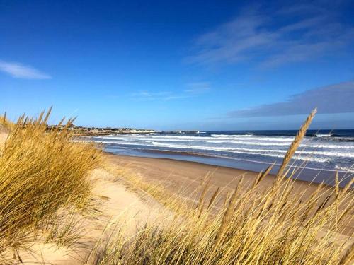 a sandy beach with waves in the ocean and grass at 3 Marina Quay in Lossiemouth