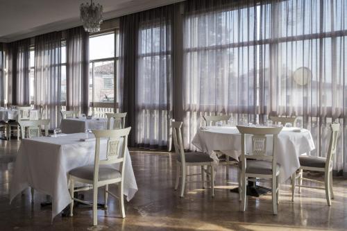 jadalnia z białymi stołami, krzesłami i oknami w obiekcie Hotel Beatrice w mieście Este