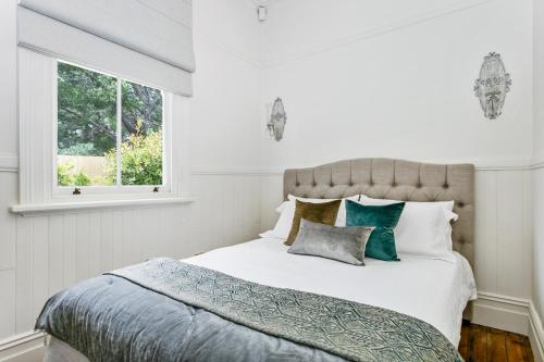 ein weißes Schlafzimmer mit einem Bett mit Kissen und einem Fenster in der Unterkunft Gowan Brae Cottage in Katoomba