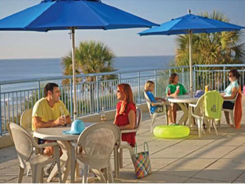 a group of people sitting at tables with blue umbrellas at Coral Beach Resort in Myrtle Beach