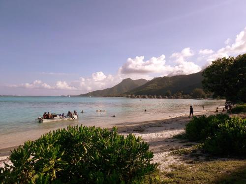people on a beach with a boat in the water at Haere Mai I Te Fare in Teavaro