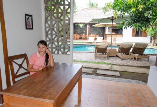 a woman sitting at a table talking on a cell phone at Si Pitung Village in Gili Air