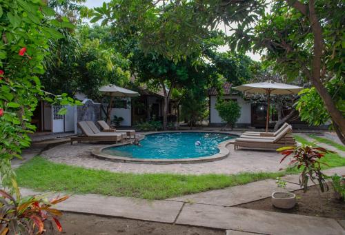a pool with chairs and umbrellas in a yard at Si Pitung Village in Gili Air