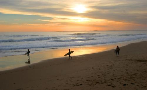 three people walking on the beach with their surfboards at Stunning Waterfront only 10 minutes to Phillip Island - FREE EV UNIT 7kW for electric cars - pet friendly, fireplace FREE WIFI wine & chocolates in Kilcunda