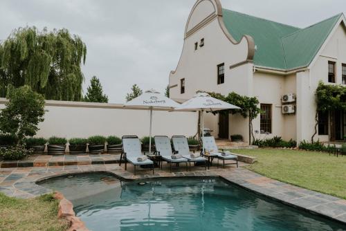 a pool with chairs and umbrellas in front of a house at Cana Vineyard Guesthouse in Paarl