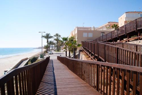 a wooden boardwalk leading to a beach with palm trees at Apartamentos Riviera Beach in Pilar de la Horadada