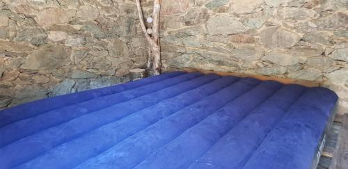niebieskie łóżko przed kamienną ścianą w obiekcie U paliaghju, une cabane de berger pour vivre un dépaysement total w mieście Santa-Lucia-di-Mercurio