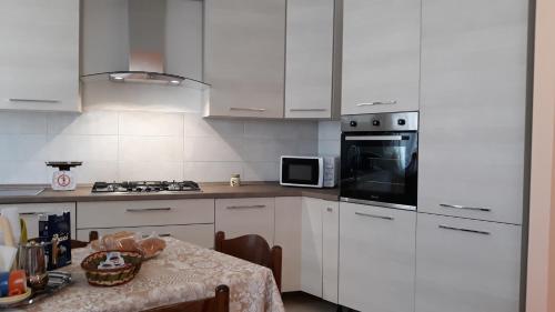 cocina con armarios blancos, mesa y microondas en Lux Appartamento, en Busso