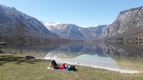 a person laying on the grass next to a lake at Snežak (Snowman) 2 in Bohinj