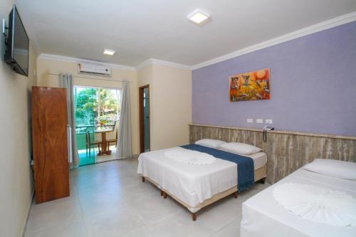 a bedroom with two beds and a tv and a balcony at Areia do Atlantico Hotel in Porto Seguro