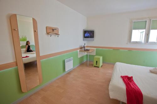a bedroom with a mirror and a woman sitting on a bed at ibis budget Marne la Vallée in Saint-Thibault-des-Vignes