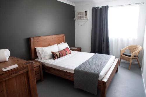 a bedroom with a bed and a chair and a window at Motel Nomad in Cairns