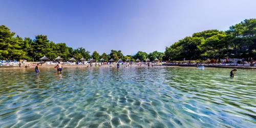 a group of people standing in the water at a beach at Pine Beach Pakostane - All Inclusive light in Pakoštane