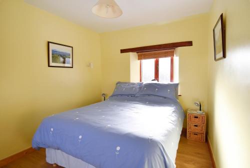 a bedroom with a bed with blue sheets and a window at Ferryman's Cottage in Glasbury