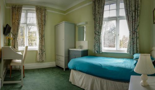 a bedroom with a blue bed and two windows at Sandfield Guest House in Oxford