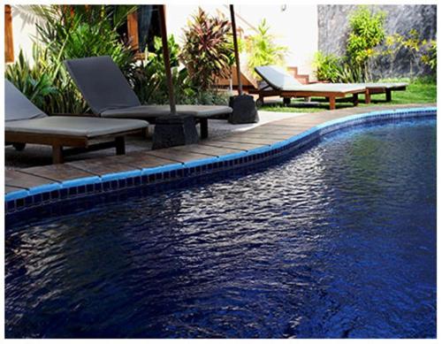 a swimming pool with two lounge chairs next to a body of water at Niramaya Villa in Seminyak