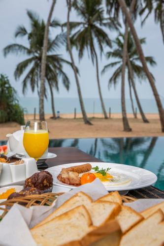 a table with a plate of food and a glass of orange juice at Serendivi Resort Villa in Tangalle