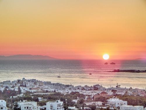 a city with the sun setting over the ocean at Panos Luxury Suite in Parikia