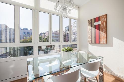 una mesa de comedor de cristal con sillas blancas y una lámpara de araña en Art House Fira Apartments en Barcelona