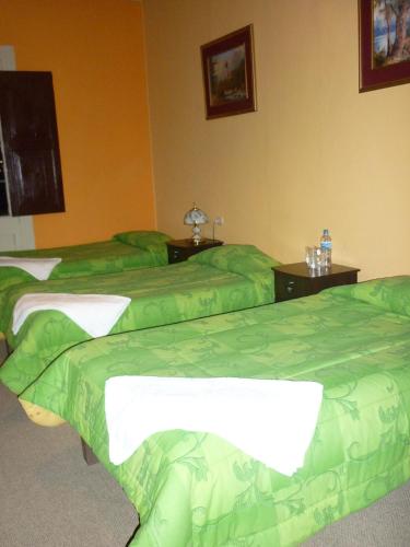 a room with three beds with green covers at Hostal Los Balcones de Moral y Santa Catalina in Arequipa