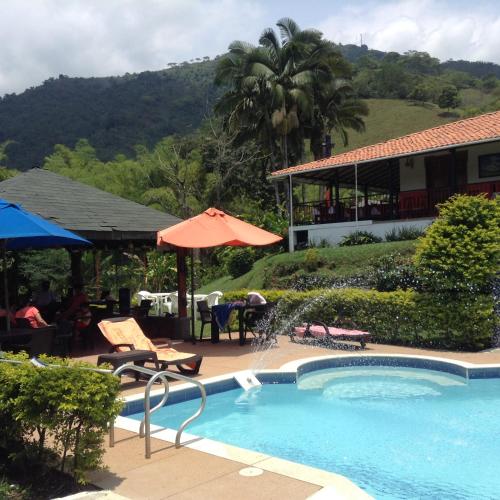 a swimming pool with an umbrella and a house at Finca El Sueño De Mi Abuelo in Pereira