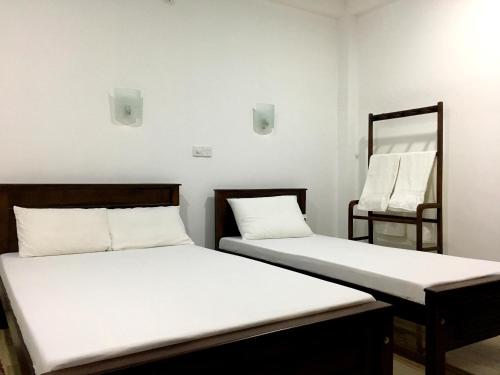 two beds in a room with white sheets and a mirror at Anthony Guesthouse in Hikkaduwa