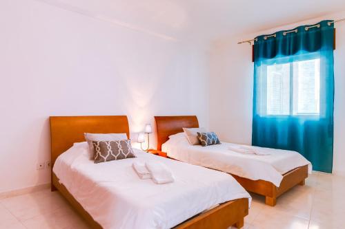 Duas camas num quarto com cortinas azuis em Rei - Quarteira - 3 min to the beach em Vilamoura