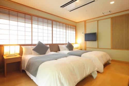2 Betten in einem Zimmer mit Fenstern und einem TV in der Unterkunft Hotel Futaba in Yuzawa