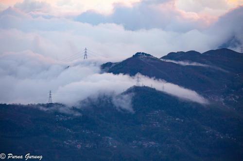a mountain covered in clouds with a city on top of it at Dreamhome Stay in Kurseong