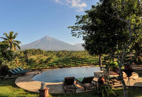 a pool with chairs and a mountain in the background at Ijen Resort and Villas - The Hidden Paradise in Banyuwangi