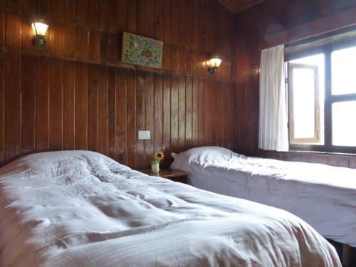 two beds in a room with wooden walls and a window at Lukla Airport Resort Lukla in Lukla